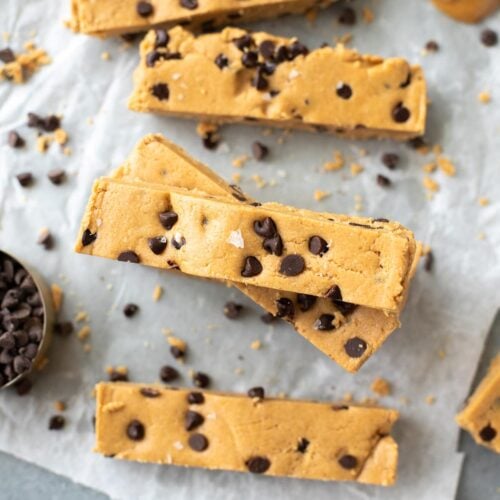 Homemade Peanut Butter Protein Bars on a piece of parchment paper with peanut butter and chocolate off to the side