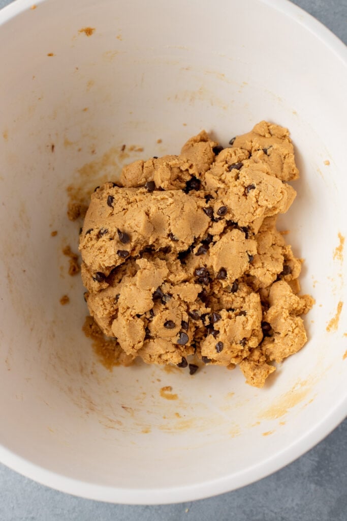 Ingredients for Peanut Butter Protein Bars in a large white bowl mixed together with chocolate chips stirred in.