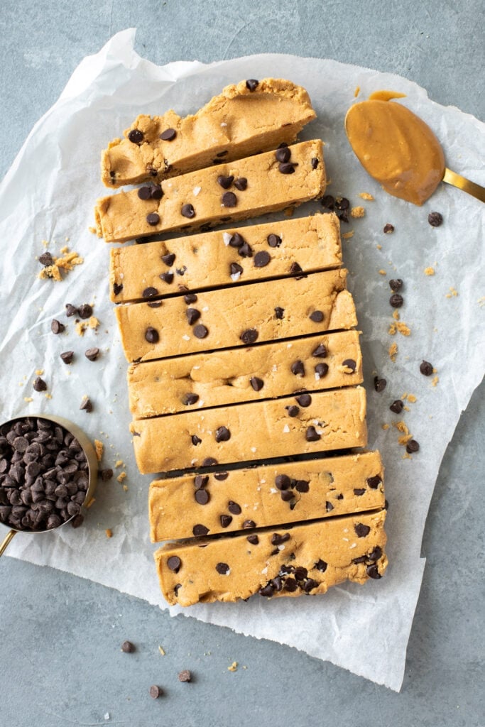 Homemade Peanut Butter Protein Bars on a parchment paper background with chocolate chips and peanut butter off to the side