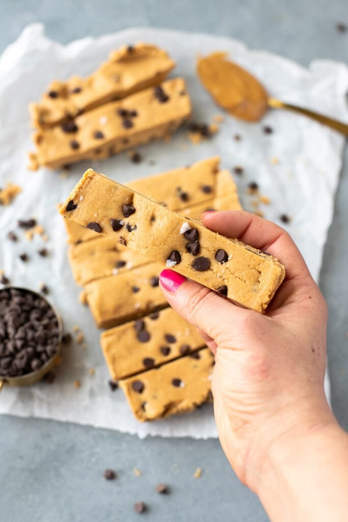 A hand holding up a copycat perfect bar to the camera - stack of protein bars can be seen in the background