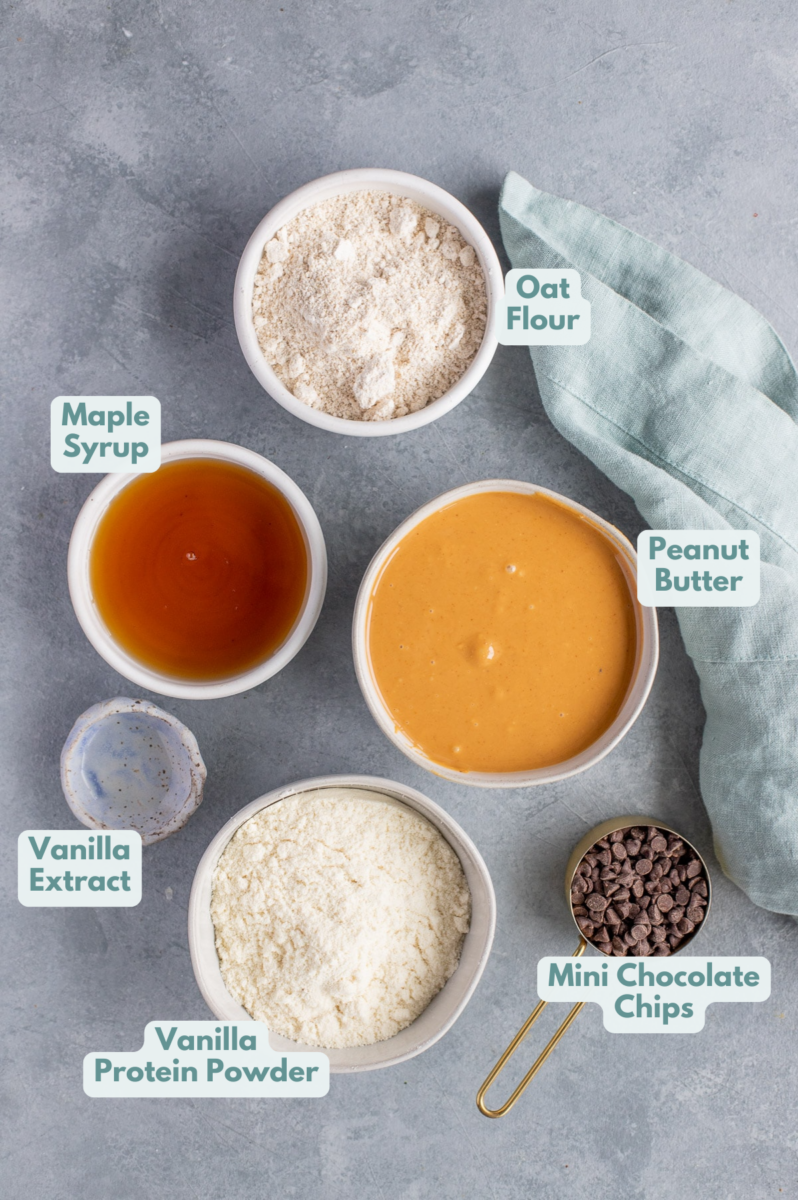 Ingredients for homemade peanut butter protein bars in small white bowls on a grey background