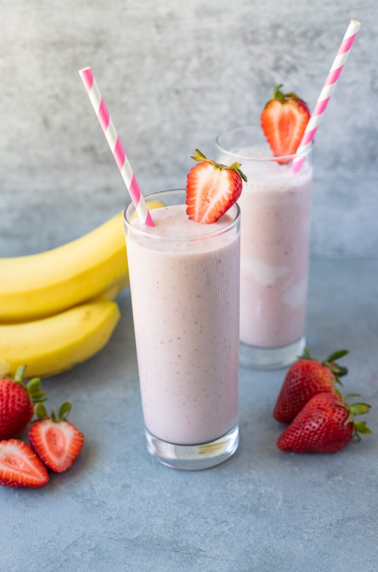 Two Strawberry Banana Smoothies in glass jars on a grey background with strawberries and bananas off to the side