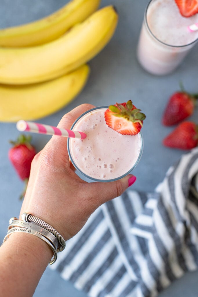 An overhead image of a hand holding a glass filled with a strawberry banana smoothie