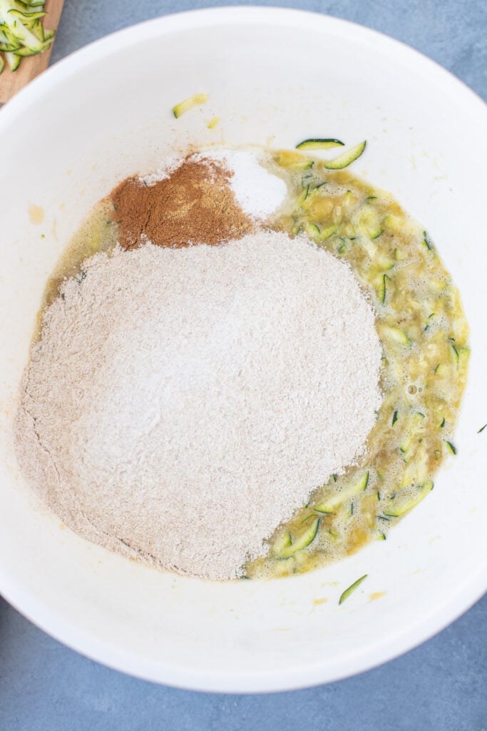 Wet ingredients for zucchini banana bread mixed together with dry ingredients being added on top with pieces of shredded zucchini in it