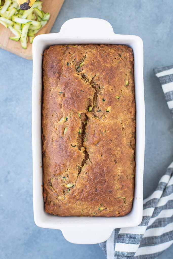 Healthy banana Zucchini Bread in a white loaf pan fresh out of the oven on a grey background