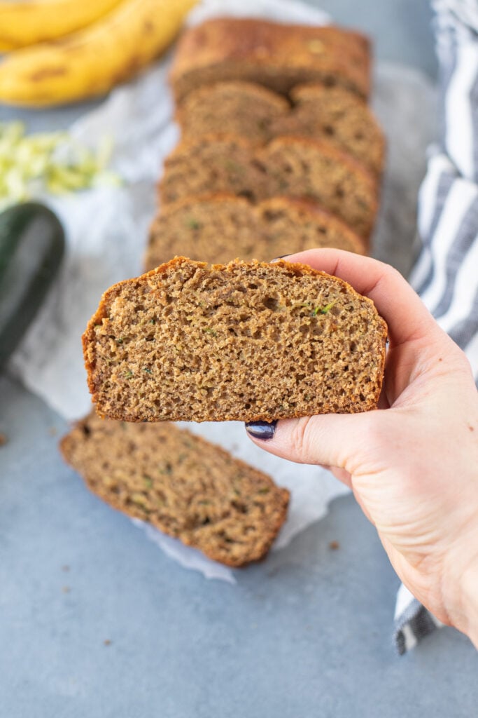 A hand holding up a slice of zucchini banana bread to the camera