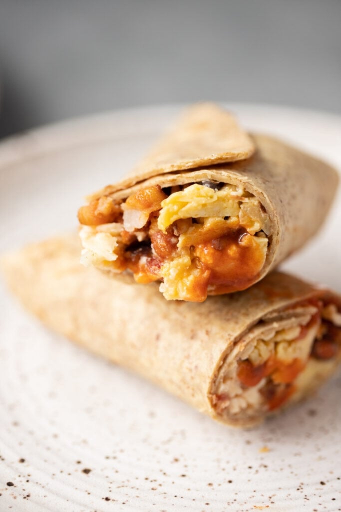 A close up of a healthy breakfast burrito on a white plate cut in half