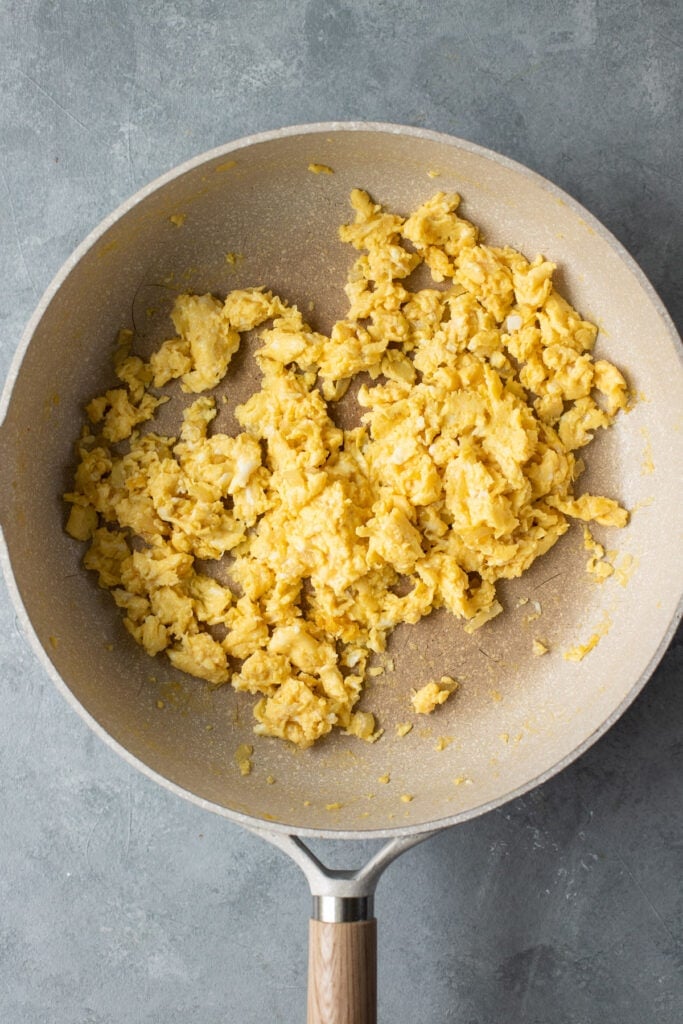 Eggs and onions being scrambled in a grey pan