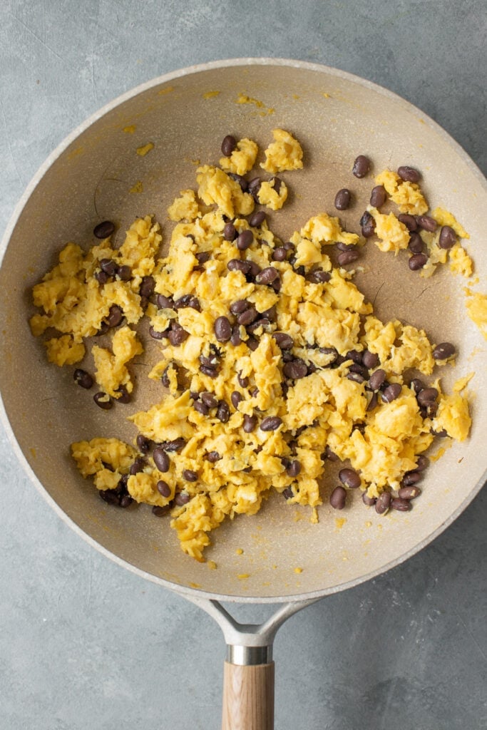 Scrambled eggs in a pan with black beans for breakfast burritos