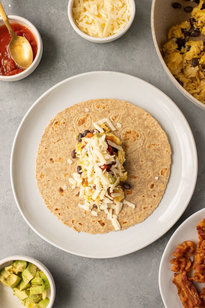 A bacon breakfast burrito on a tortilla before being rolled up