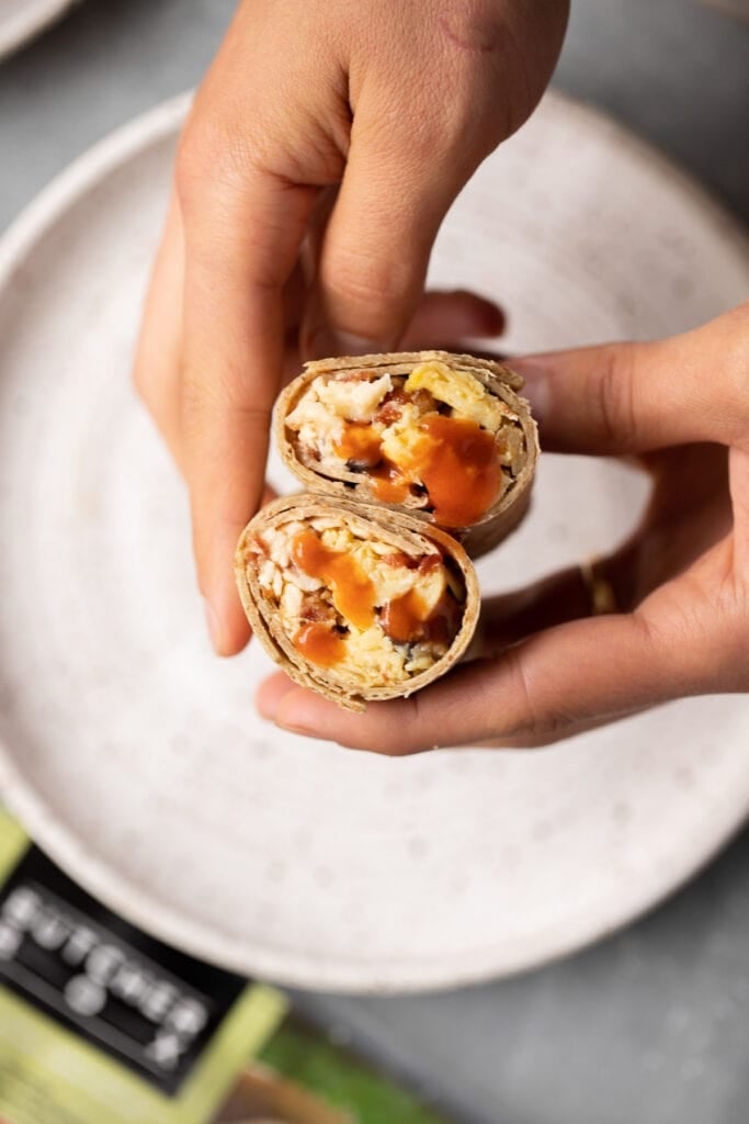 Two hands holding a breakfast burrito cut in half