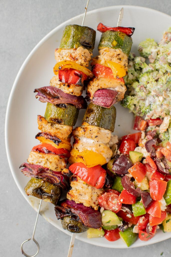 Greek Chicken Kabobs on a plate with broccoli salad off to the side