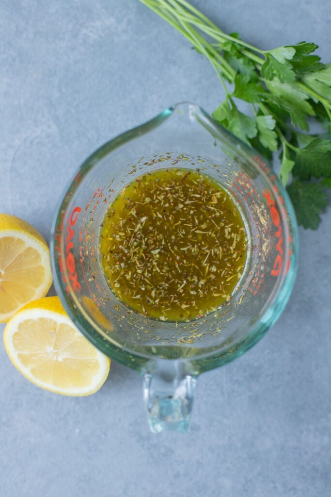 Greek Chicken Marinade whisked together in a glass measuring cup on a grey background