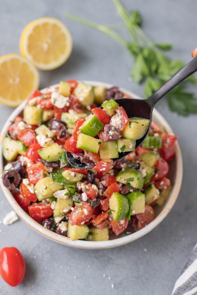 A black spoon taking a scoop out of greek salad
