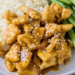 A close up of healthy orange chicken on a white plate with green beans and rice on the side.