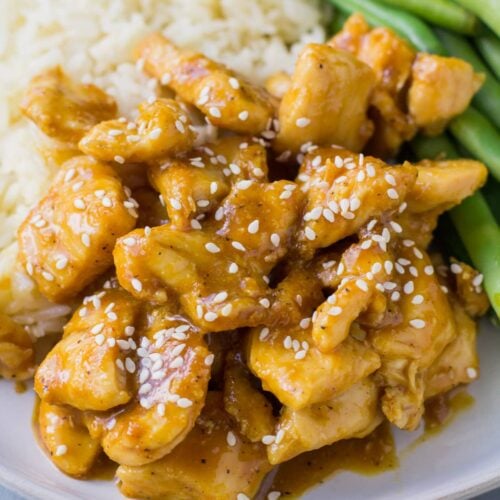 A close up of healthy orange chicken on a white plate with green beans and rice on the side.