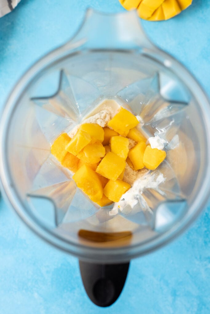 ingredients for a mango smoothie in a blender before being blended