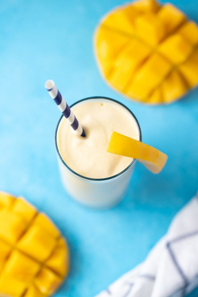 A healthy mango smoothie on a blue background with a bright blue straw off to the side