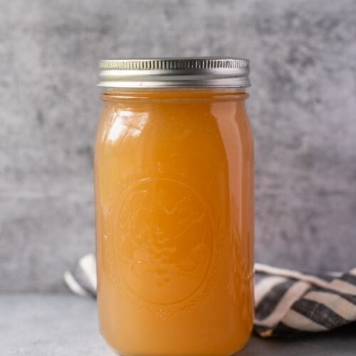 Bee Bone Broth in a glass jar on a grey background with a lined linen in the back