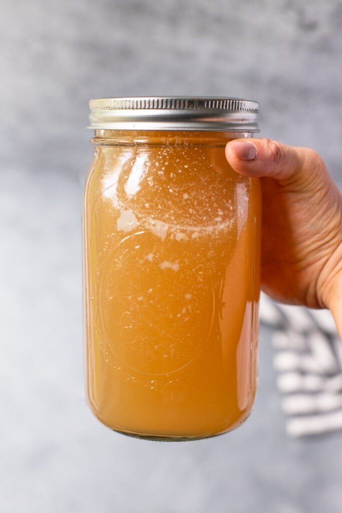 A hand holding up a jar of homemade beef bone broth from scratch