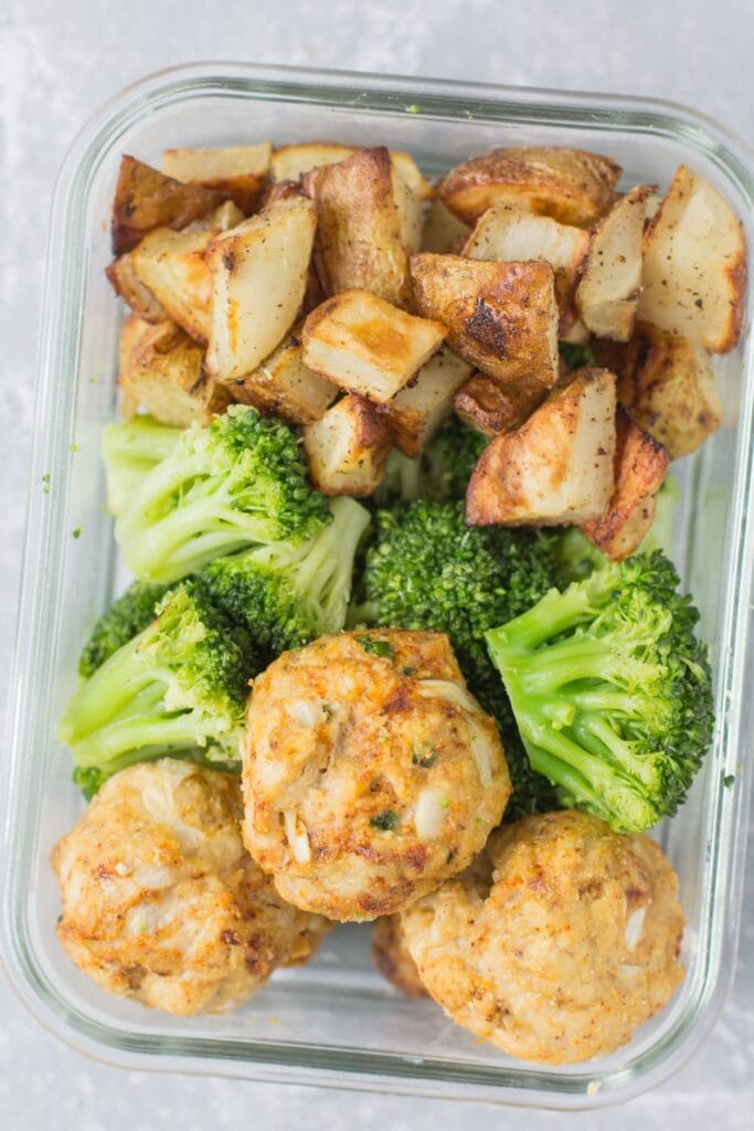 Meal prep meatballs, steamed broccoli and roasted potatoes in a glass container on a grey background