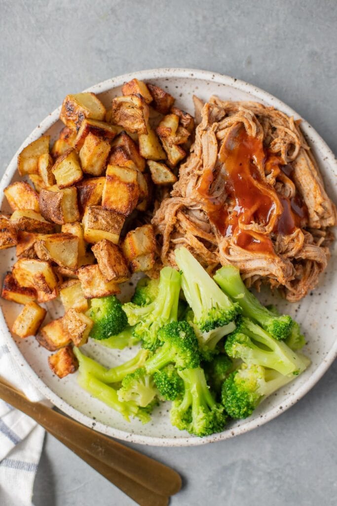 Healthy Meal Prep Idea - Crockpot Pulled Pork in a white dish with roasted potatoes and broccoli off to the side