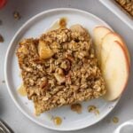A close up of healthy baked oatmeal on a white plate with apples off to the side