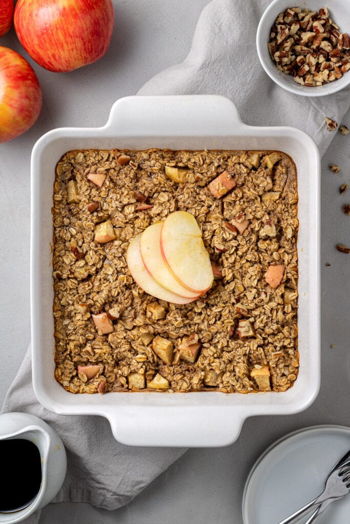 An overhead image of apple baked oatmeal in a white baking dish with ingredients off to the side