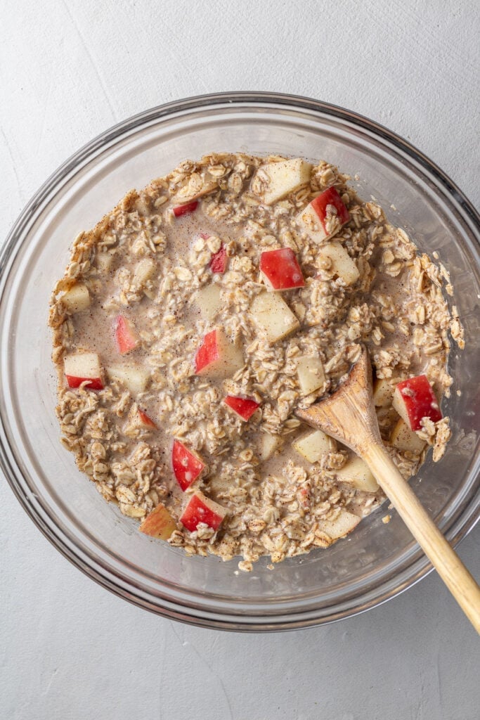 An overhead image of baked oatmeal batter being mixed together in a glass bowl with a wooden spoon