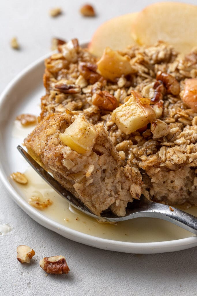 A fork taking a bite out of healthy apple baked oatmeal on a white plate