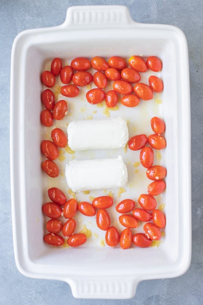 Goat cheese and tomatoes in a white baking dish before being baked