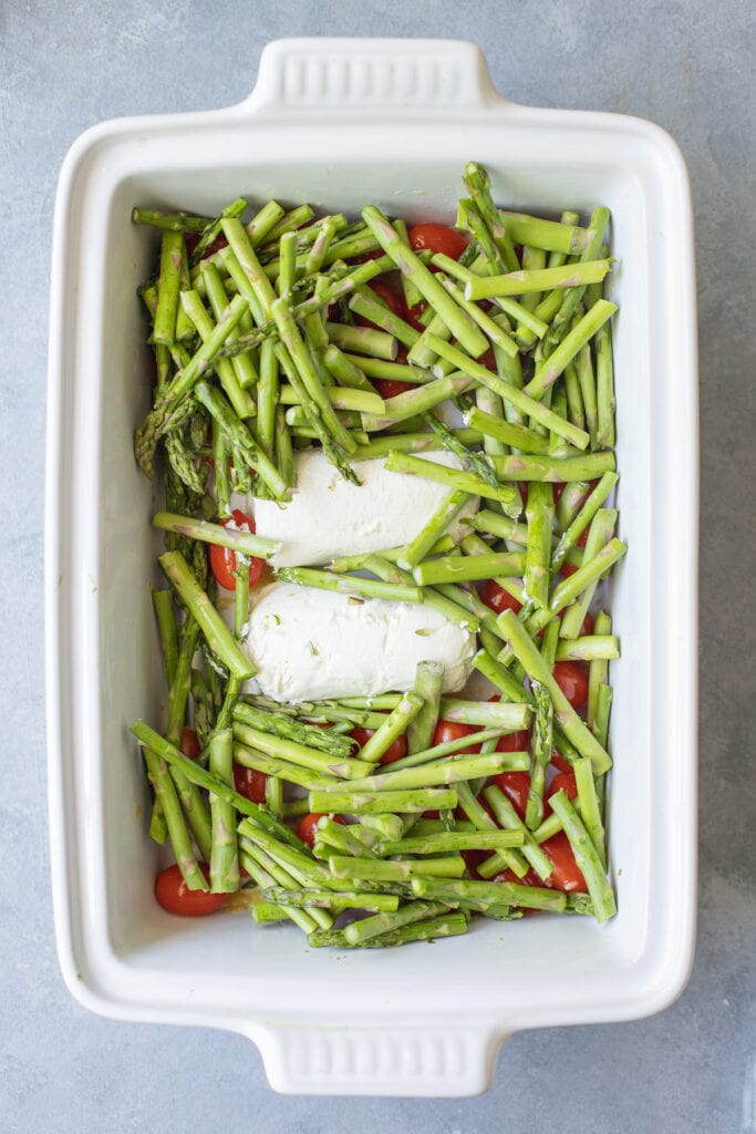 Asparagus being added to a white baking dish for goat cheese pasta