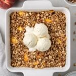 an overhead shot of healthy peach crisp in a white baking dish on a grey background
