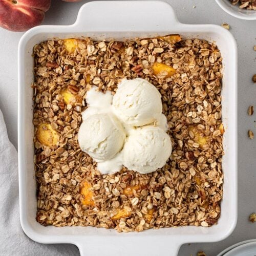 an overhead shot of healthy peach crisp in a white baking dish on a grey background