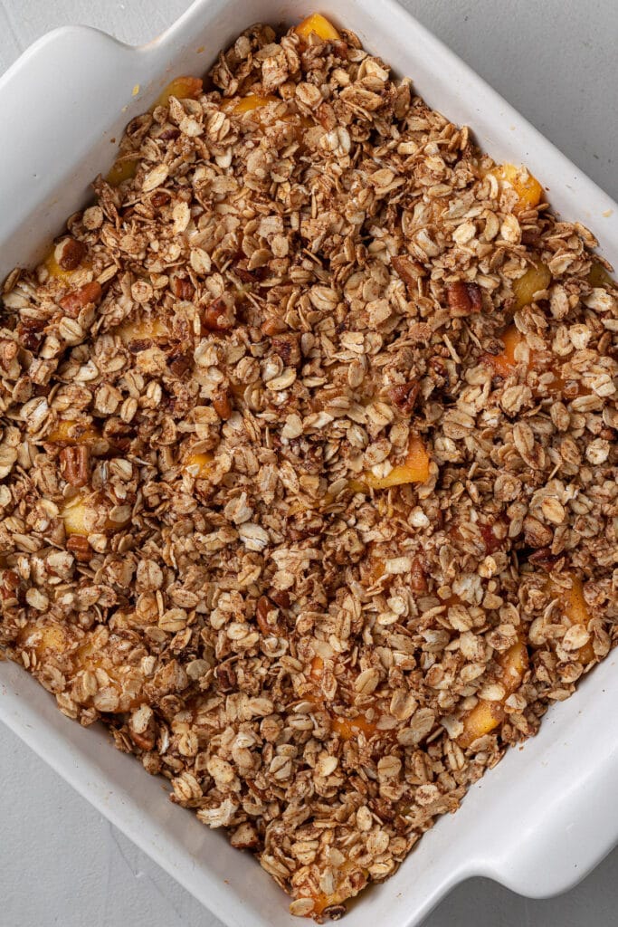 healthy peach crisp in a white baking dish before going into the oven