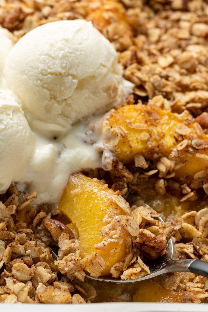 A close up of easy peach crisp fresh out of the oven with ice cream on top