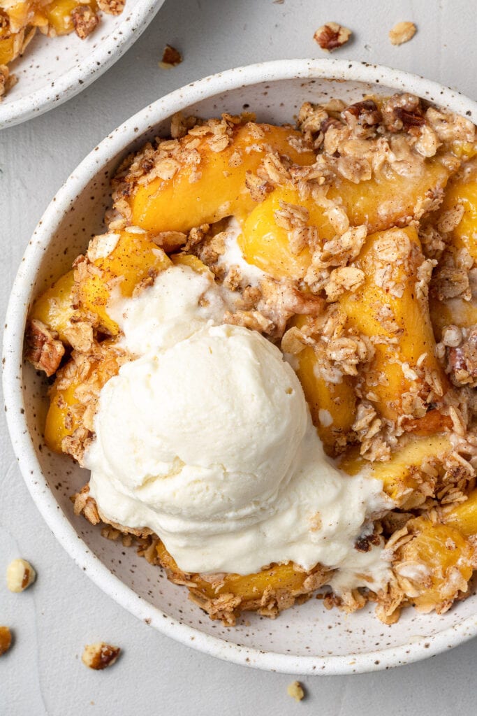 A bowl of easy peach crisp white a scoop of vanilla ice cream on top