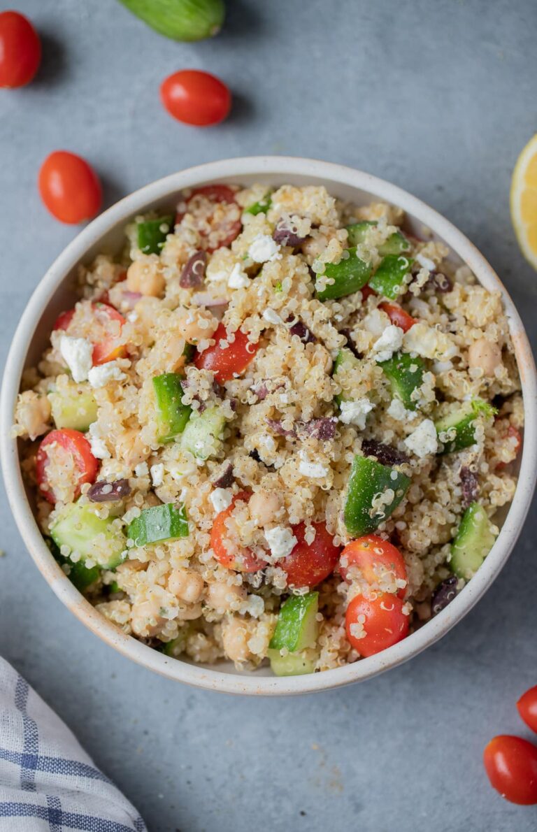A bowl of Mediterranean Quinoa Salad on a grey background with tomatoes off to the side.