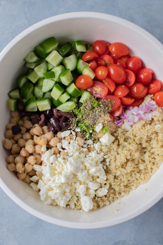 Quinoa Salad in a white bowl on a grey background before being stirred together