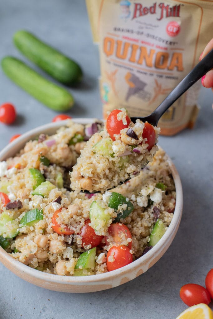 A close up of quinoa salad with a spoon scooping a serving out of it.