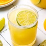 A close up of a skinny margarita on a white background with sliced citrus in the background