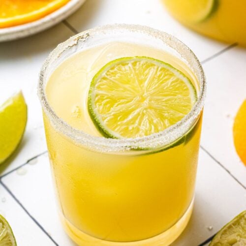 A close up of a skinny margarita on a white background with sliced citrus in the background
