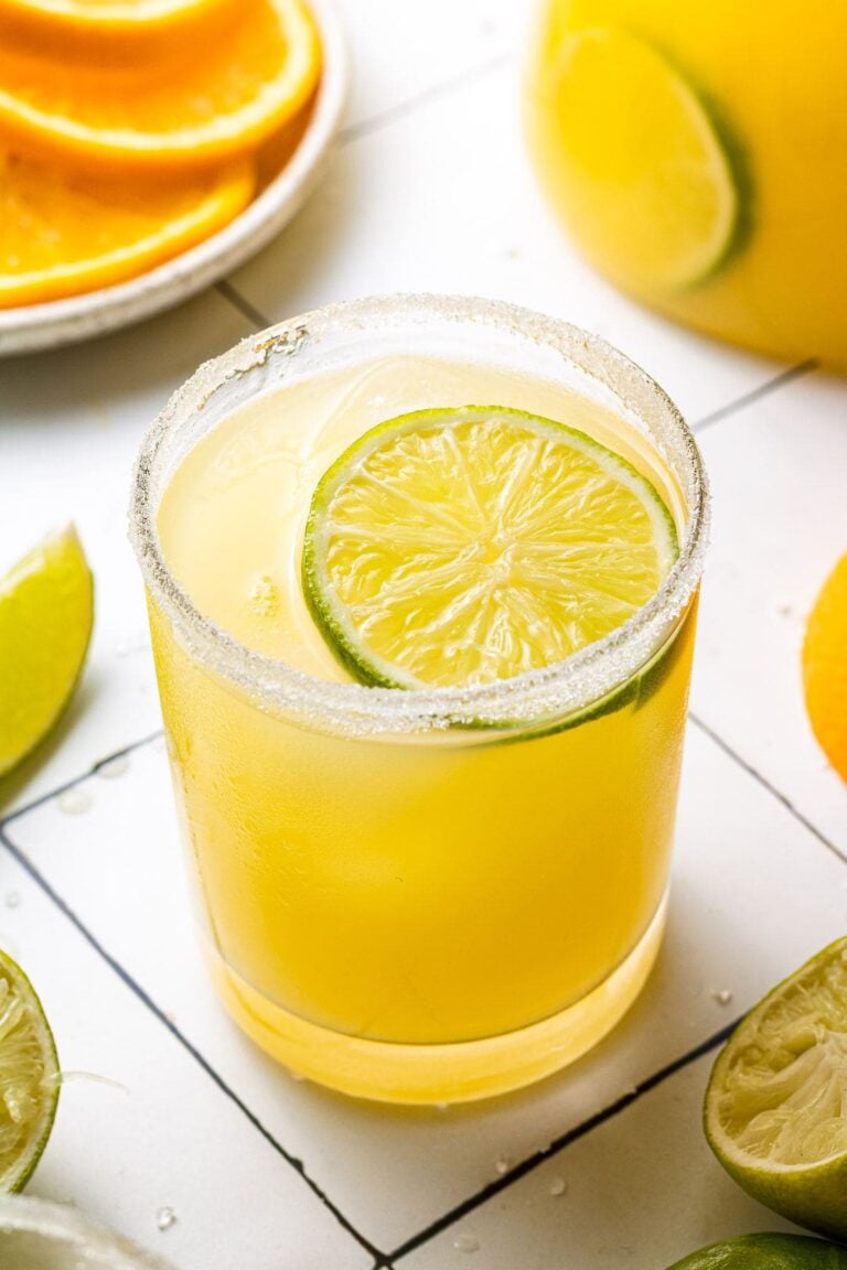 A close up of a skinny margarita on a white background with sliced citrus in the background