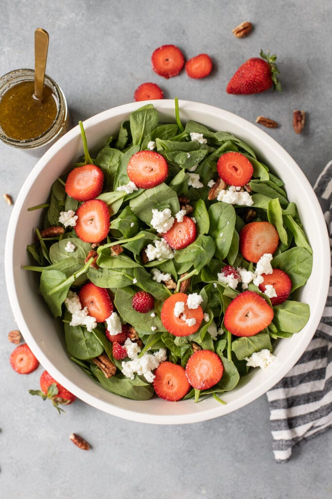 An overhead shot of strawberry spinach salad in a white bowl on a grey background