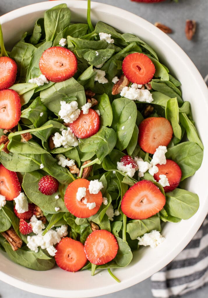 a close up of Strawberry spinach salad in a white bowl on a grey background