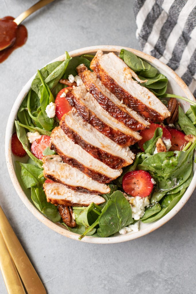 an overhead image of strawberry spinach salad with grilled chicken on top