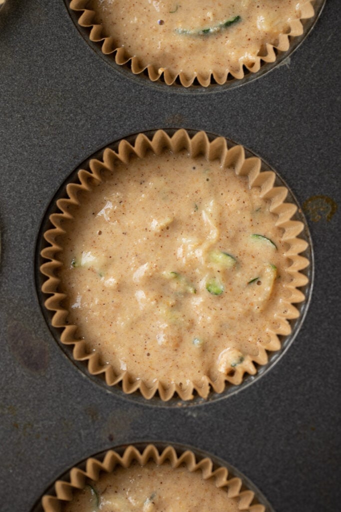 A lined muffin tin with raw zucchini muffin batter