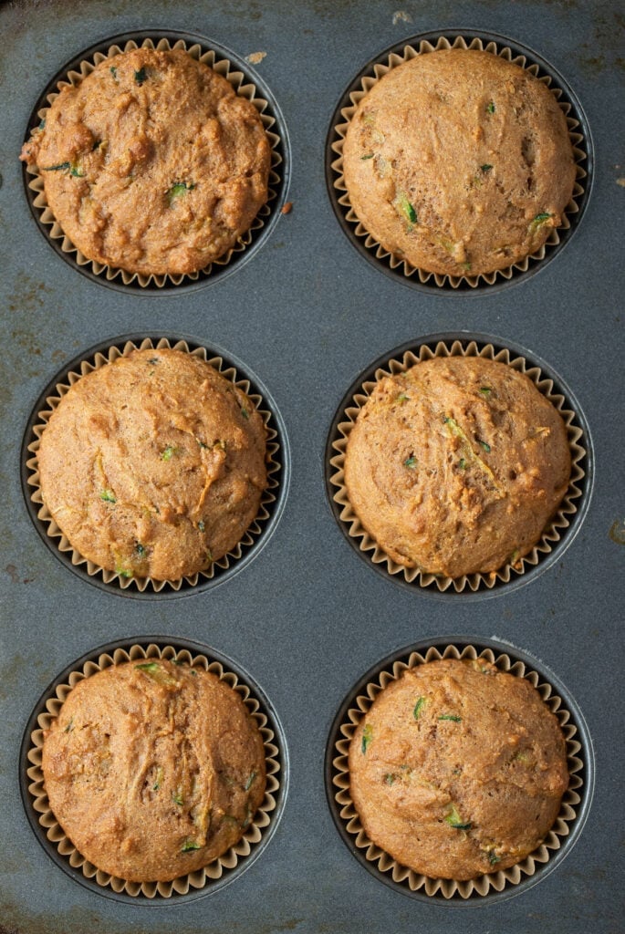 Six freshly baked healthy zucchini muffins still in the tins