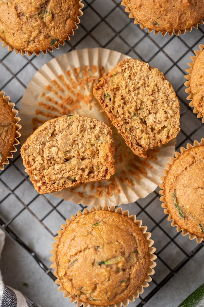 Healthy zucchini muffins on a wire rack on a grey background with one muffin cut in half