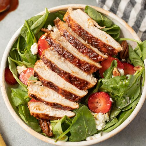 A close up of BBQ Chicken breasts sliced on top of a salad